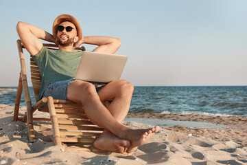 Man with laptop relaxing in deck chair on beach