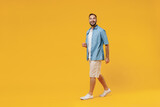 Fototapeta Lawenda - Full body young smiling happy cheerful satisfied caucasian man 20s wearing blue shirt white t-shirt walking going stroll isolated on plain yellow background studio portrait. People lifestyle concept.