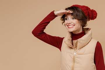 Poster - Young smiling happy caucasian woman 20s wears red turtleneck vest beret hold hand at forehead look far away distance isolated on plain pastel beige background studio portrait People lifestyle concept