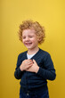 Cheerful caucasian boy kid wearing casual clothes smiling with hands on chest with closed eyes and grateful gesture on face. health concept. isolated over yellow studio background, copy space