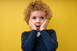 Little surprised child boy in shock, touching cheeks, stand with widely opened mouth and eyes, looking at side, saw something interesting, isolated on yellow studio background. copy space
