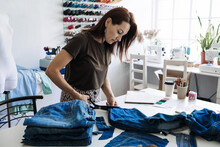 Denim Upcycling Ideas, Using Old Jeans, Repurposing Jeans, Reusing Old Jeans, Upcycle Stuff. Woman Seamstress Cut And Repair Old Blue Jeans In Sewing Studio.