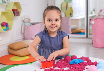 Poster - Cute little girl playing with bright kinetic sand at table in room