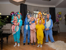 Kids in kigurumi pyjamas posing together near party table with chips and cake