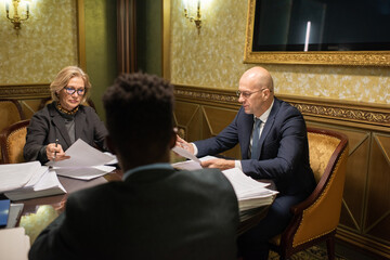 Poster - Group of intercultural contemporary lawyers in formalwear gathered by table in stylish boardroom for working meeting