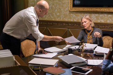 Aufkleber - Bald businessman in formalwear bending over table while passing paper to his mature female colleague at working meeting