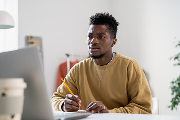 Poster - Tense young man with pencil looking at laptop screen while making notes and listening to teacher during online lesson