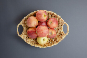 A wicker vase with beautiful red apples on a matte gray background in the center of the frame. Top view