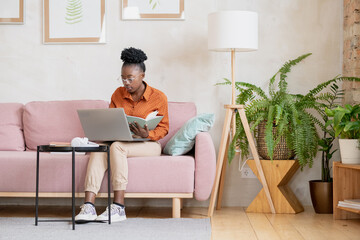Aufkleber - AFrican girl in casualwear sitting on couch against wall in living-room and making notes during online lesson