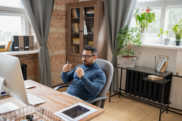 Poster - Serious teacher in casualwear listening to online student while sitting in armchair in front of computer monitor during online lesson