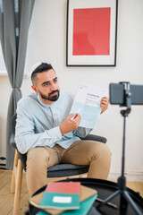 Aufkleber - Young confident man pointing at paper and looking at smartphone camera while explaining information to online audience during training