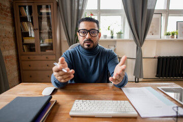 Poster - Confident middle-aged man in eyeglasses and blue pullover explaining subject to online audience in front of computer