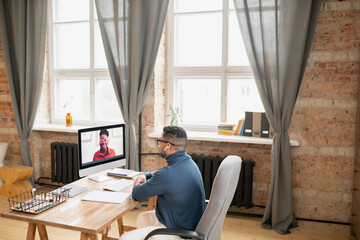 Poster - Contemporary teacher sitting by workplace in front of computer monitor and listening to African female student during online lesson