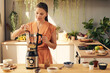 © pressmaster - Young woman putting all the ingredients for homemade smoothie or dessert into electric blender while cooking in the kitchen