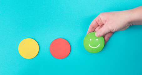 Wall Mural - Hand holds a green smiling face, red and yellow circle empty, blue colored background, copy space, customer review