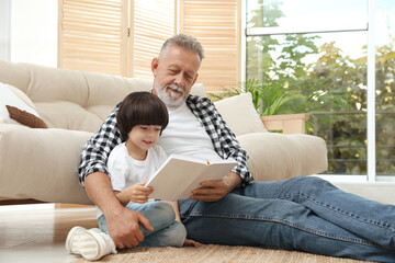 Wall Mural - Happy grandfather with his grandson reading book together at home