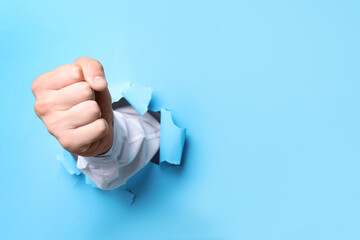 Wall Mural - Businessman breaking through light blue paper with fist, closeup. Space for text