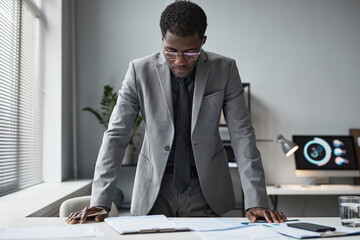 Portrait of successful black businessman leaning over desk in office and reading document, copy space