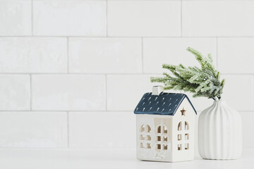 Wall Mural - Christmas greeting card design. Small ceramic house and vase with fir branch on white table. Scandinavian style Christmas home decor.