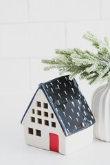 Wall Mural - Little ceramic house Christmas decoration and fir branch on white table. Happy winter holidays concept.