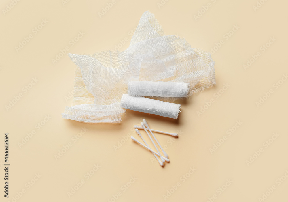 Medical gauze rolls and cotton buds on color background