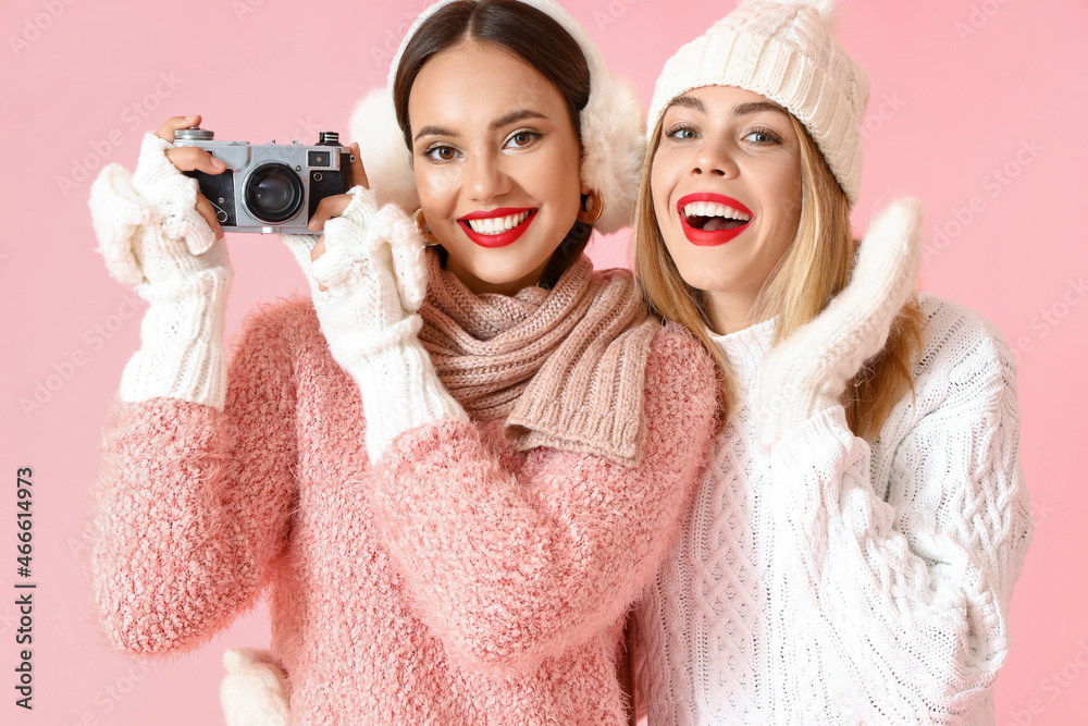 Beautiful sisters with photo camera on pink background