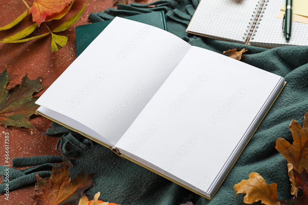 Blank open book and autumn leaves on color background, closeup