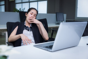 Tired sleepy asian woman yawning working at office desk. overwork and sleep deprivation concept.