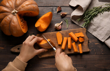 Woman cutting fresh pumpkin on wooden background