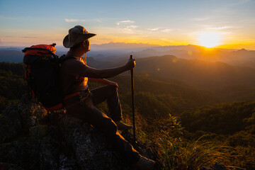 Wall Mural - young man hiker on a top of a mountain standing on top of cliff in summer mountains at sunset and en