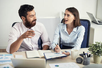 Wall Mural - Inspired young business people sitting at table with papers and analyzing statistics while working together