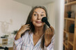 © shurkin_son - Picture of usual daily morning of average mature business woman standing in front of mirror doing make-up, applying blusher with special face brush enjoying moments on her own. Aging gracefully