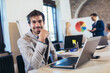 © Mediteraneo - Happy businessman using laptop with team discussing project in the background.