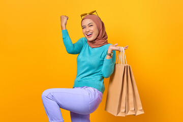 Excited and cheerful young Asian woman holding shopping bags on yellow background