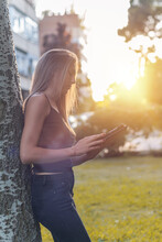 Pretty Young Blonde Woman Using A Tablet At Sunset In A Park