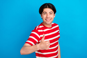 Poster - Photo of funky charming young man wear striped t-shirt smiling showing thumb up isolated blue color background