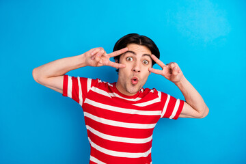 Poster - Photo of cute shocked young man wear striped t-shirt showing v-signs cover eyes isolated blue color background