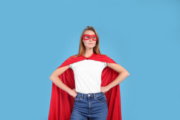 Confident woman wearing superhero cape and mask on light blue background