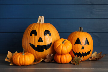 Orange pumpkins and two with drawn spooky faces on wooden table. Halloween celebration