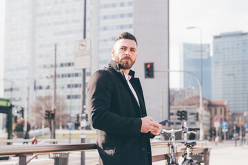 Young handsome caucasian bearded man outdoor using smartphone overlooking texting message communicating