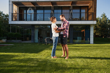 Bearded man talking with charming Caucasian female in front of the modern house