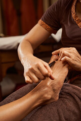 Wall Mural - Masseuse stimulating pressure point on patient foot with wooden tool