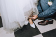 © shchus - The groom, the man helps with his hands, fastens the white shoes on the bride's leg. Wedding photography.