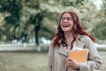 Beautiful happy 30 years businesswoman with glasses relaxing, looking in a park holding a notebooks outdoors in a city park in summer outdoors, education concept