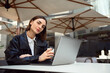 © Taras Grebinets - Fashionable woman with stylish short haircut, in white casual shirt and eco leather jacket, resting at the summer terrace of a cafe, drinking coffee, working on laptop, looking confidently at camera
