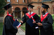 © Тарас Нагирняк - Three gradutes friends in graduation robes speaking in campus with diploma in their hands