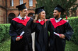 © Тарас Нагирняк - Hyppy smiling three graduates walking in university campus and celebrating graduation