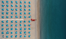 Aerial View Of A Well Sorted Lido With Blue Parasols And Sunbeds At Sunrise Along The Coastline In Calabria, Italy.