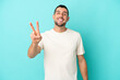 © luismolinero - Young handsome caucasian man isolated on blue background smiling and showing victory sign