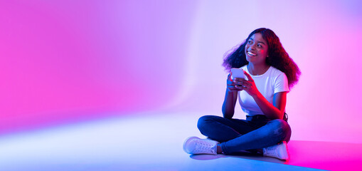 Poster - Amazing application. Young black lady using modern smartphone and looking at copy space in neon light